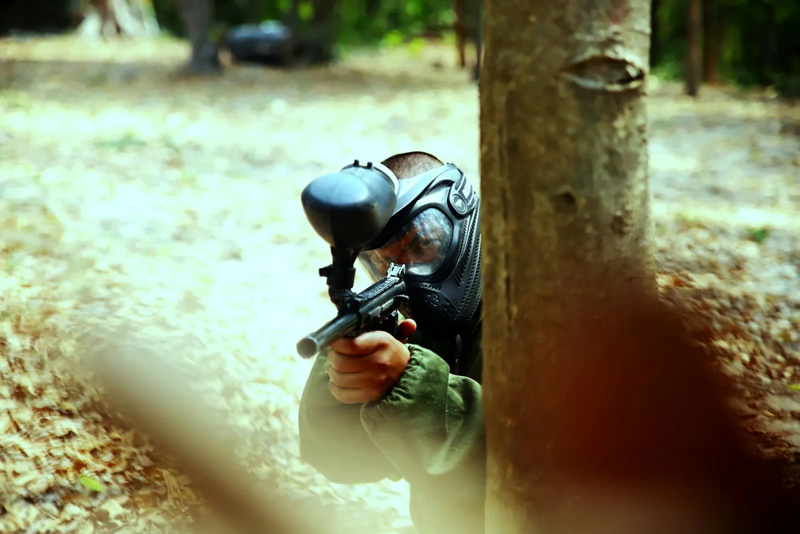 Joueur de paintball masqué tirant à l'abri d'un tronc d'arbre en forêt
