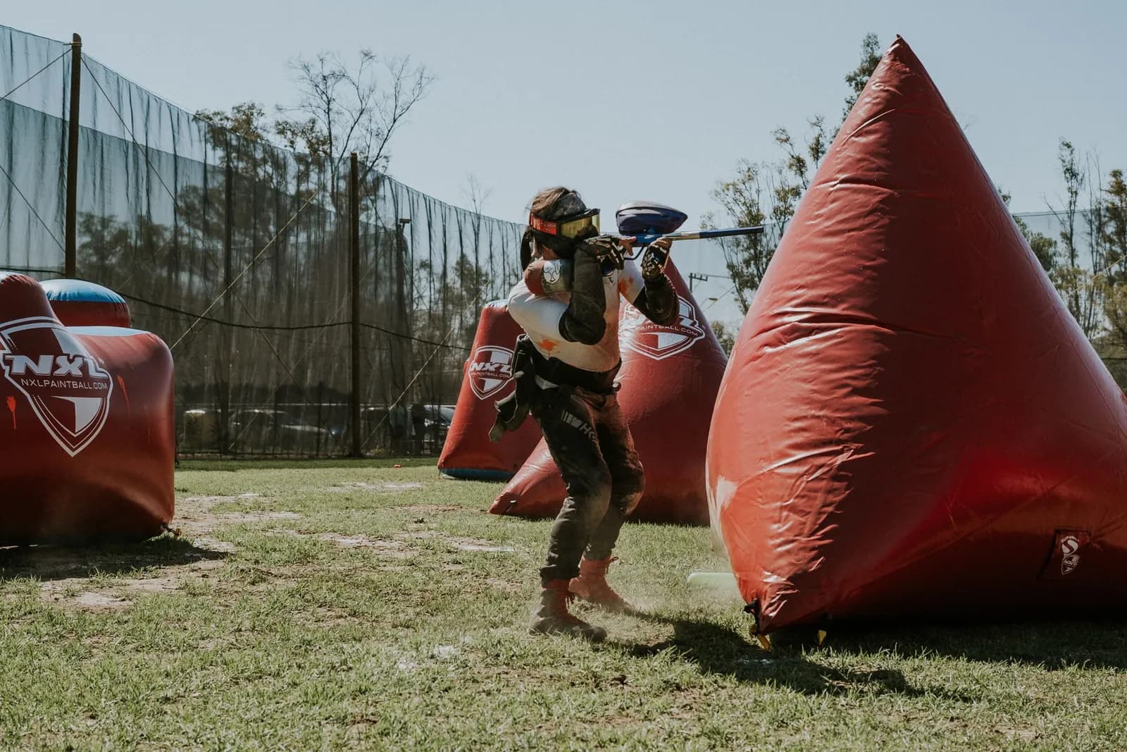 Joueur de paintball se déplaçant entre des obstacles gonflables rouges sur un terrain