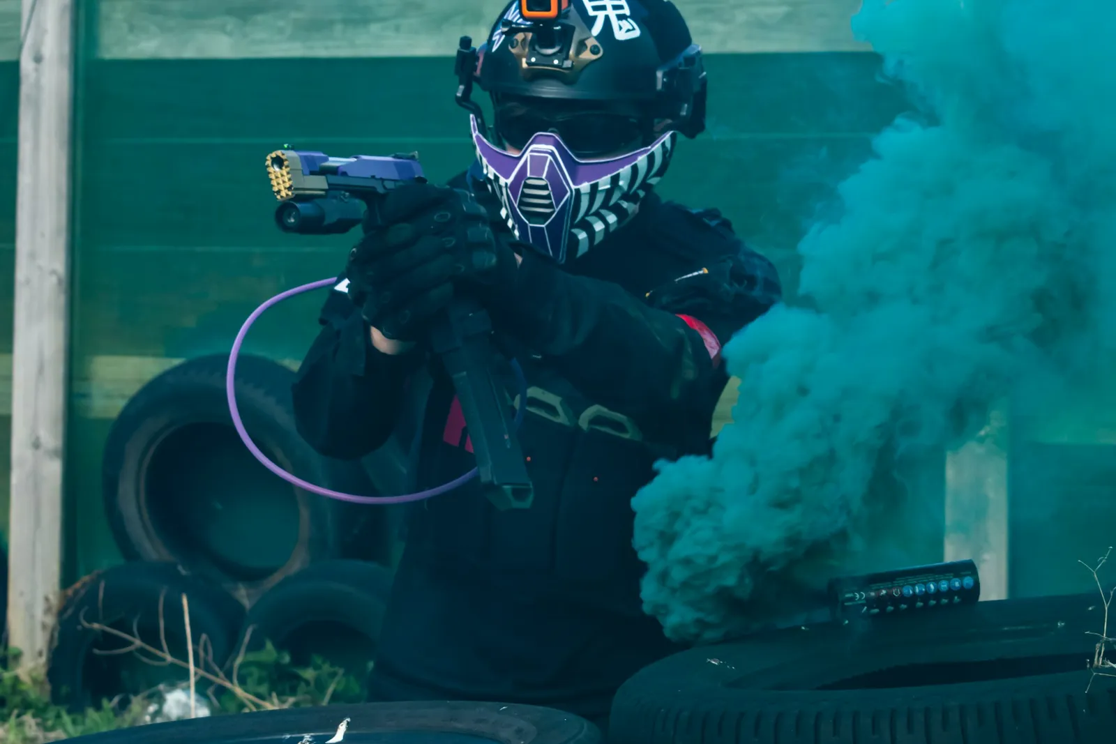 Joueur de paintball masqué derrière une barricade de pneus, au milieu d'un nuage de fumée bleue