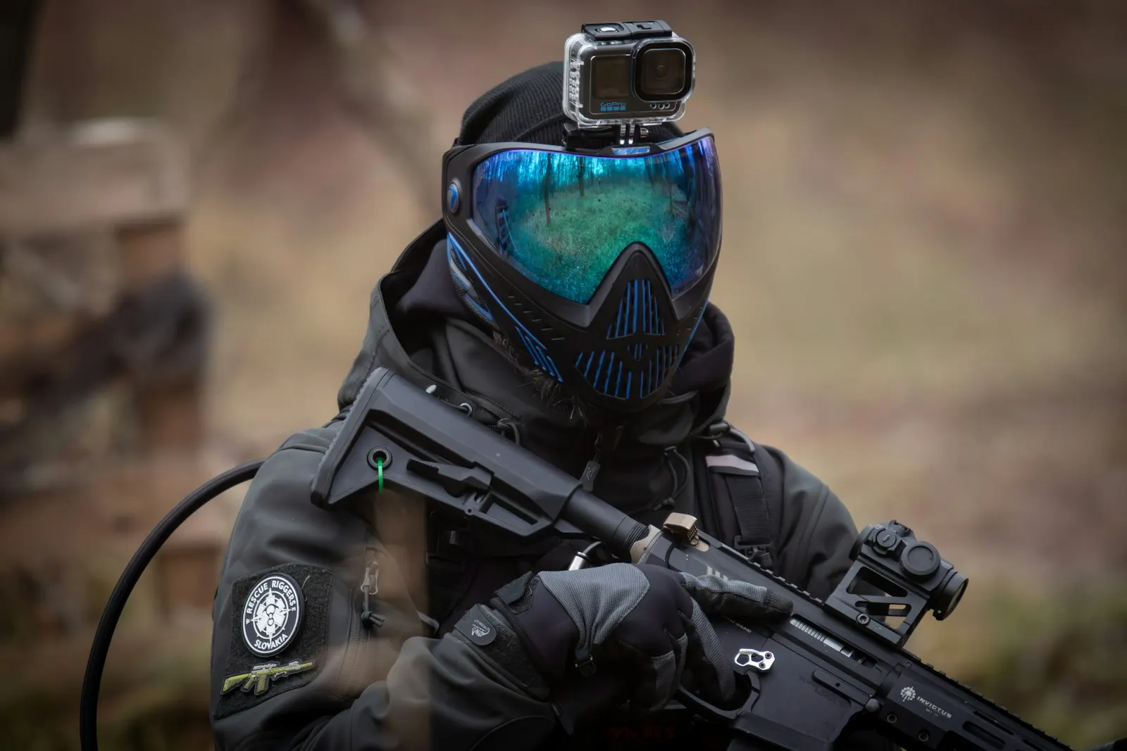 Joueur d'airsoft portant un masque de protection intégrale à écran bleu et une caméra sur la tête, réplique en main