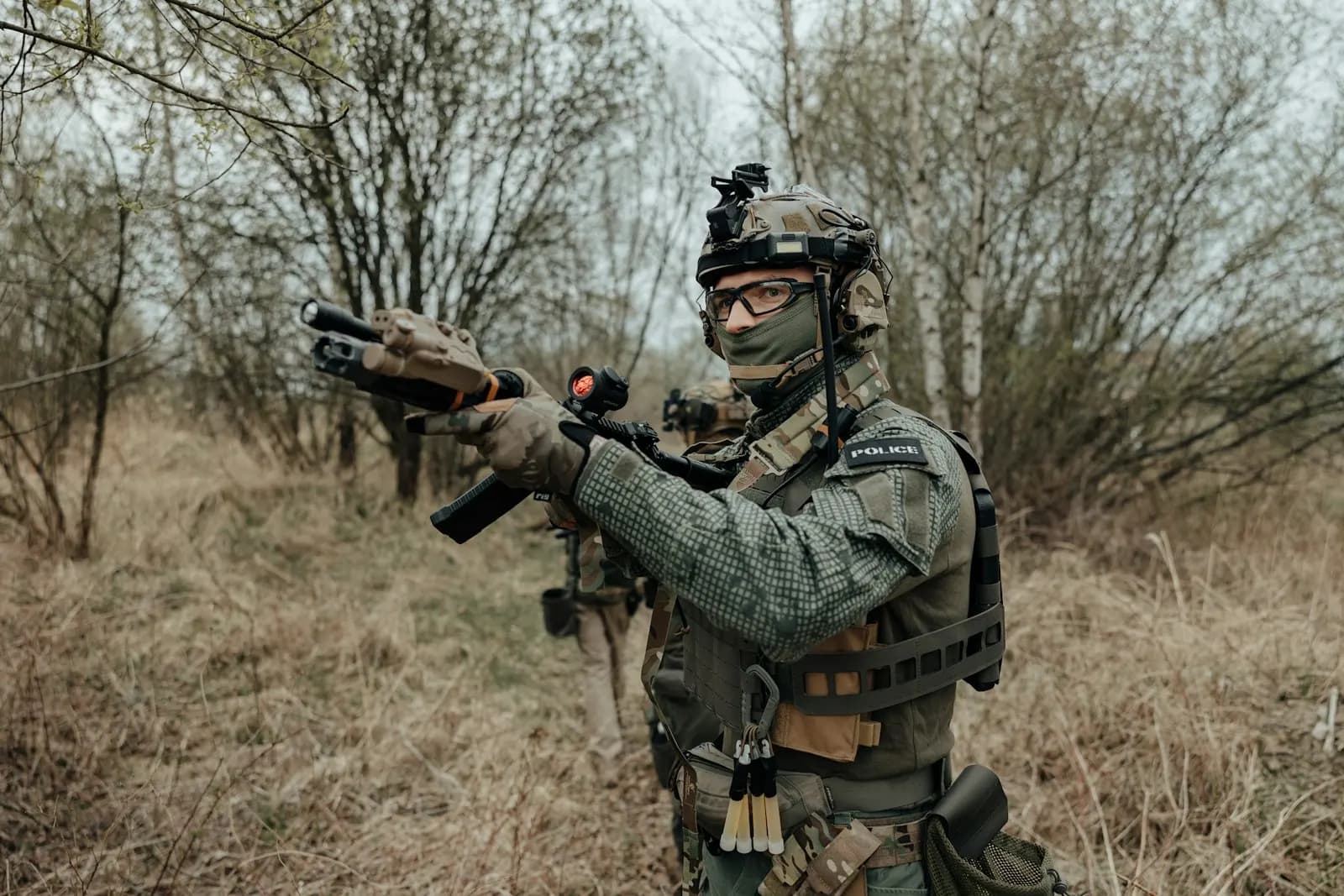 Joueur d'airsoft équipé de lunettes de protection, d'un masque bas de visage et d'un casque, réplique en main dans un sous-bois