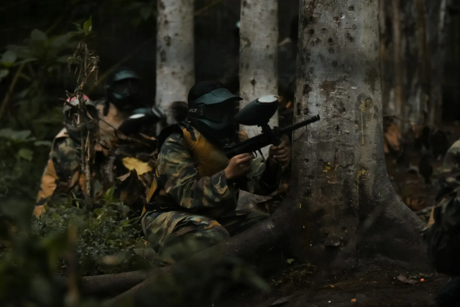 Groupe de joueurs de paintball en tenue camouflage, masques sur le visage, à couvert derrière des arbres en forêt