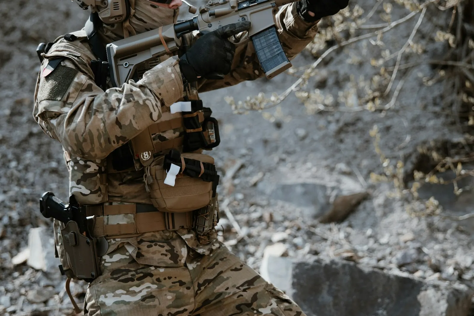 Joueur d'airsoft en tenue camouflage désert progressant sur un terrain rocailleux, réplique en main
