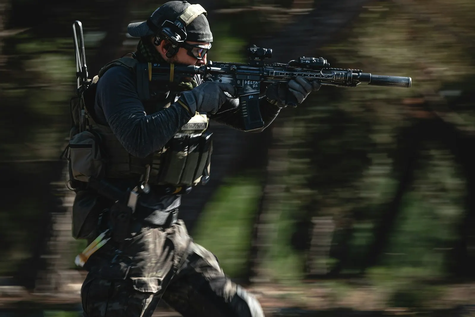 Joueur d'airsoft en tenue noire et casque courant réplique en main à travers un sous-bois
