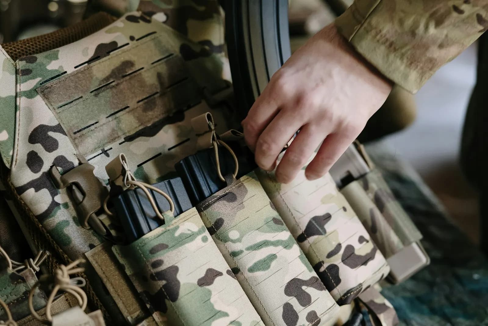 Joueur d'airsoft rangeant ses chargeurs dans les poches d'un gilet porte-plaques camouflage