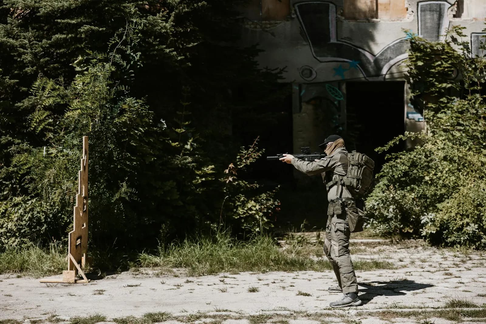 Joueur d'airsoft tirant vers une cible en bois sur un terrain extérieur pour régler sa réplique