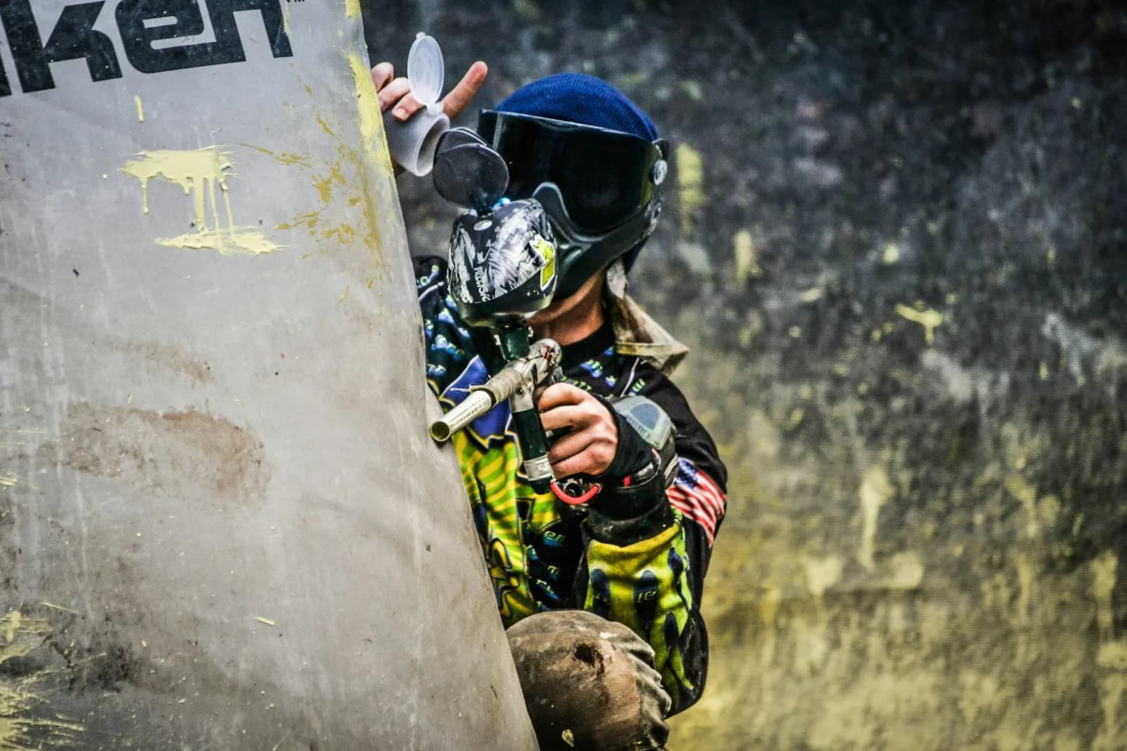 Joueur de paintball à l'abri d'un obstacle couvert d'impacts de peinture jaune