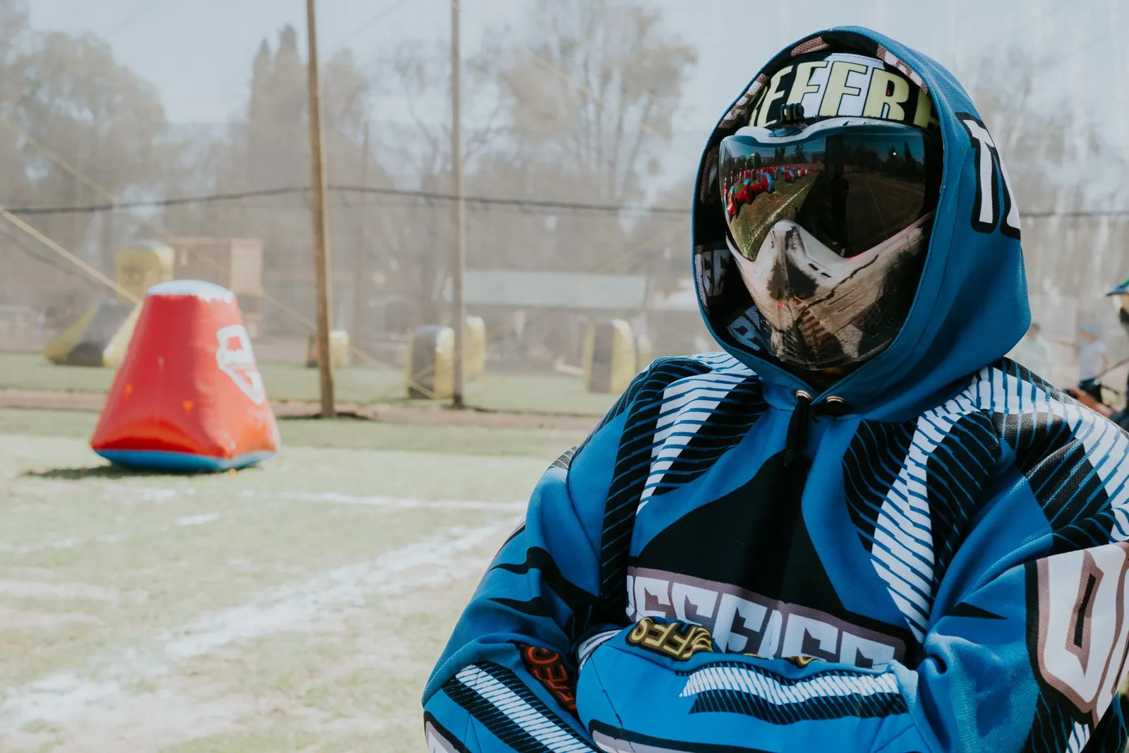 Joueur de paintball en sweat bleu et masque intégral sur un terrain avec obstacles gonflables