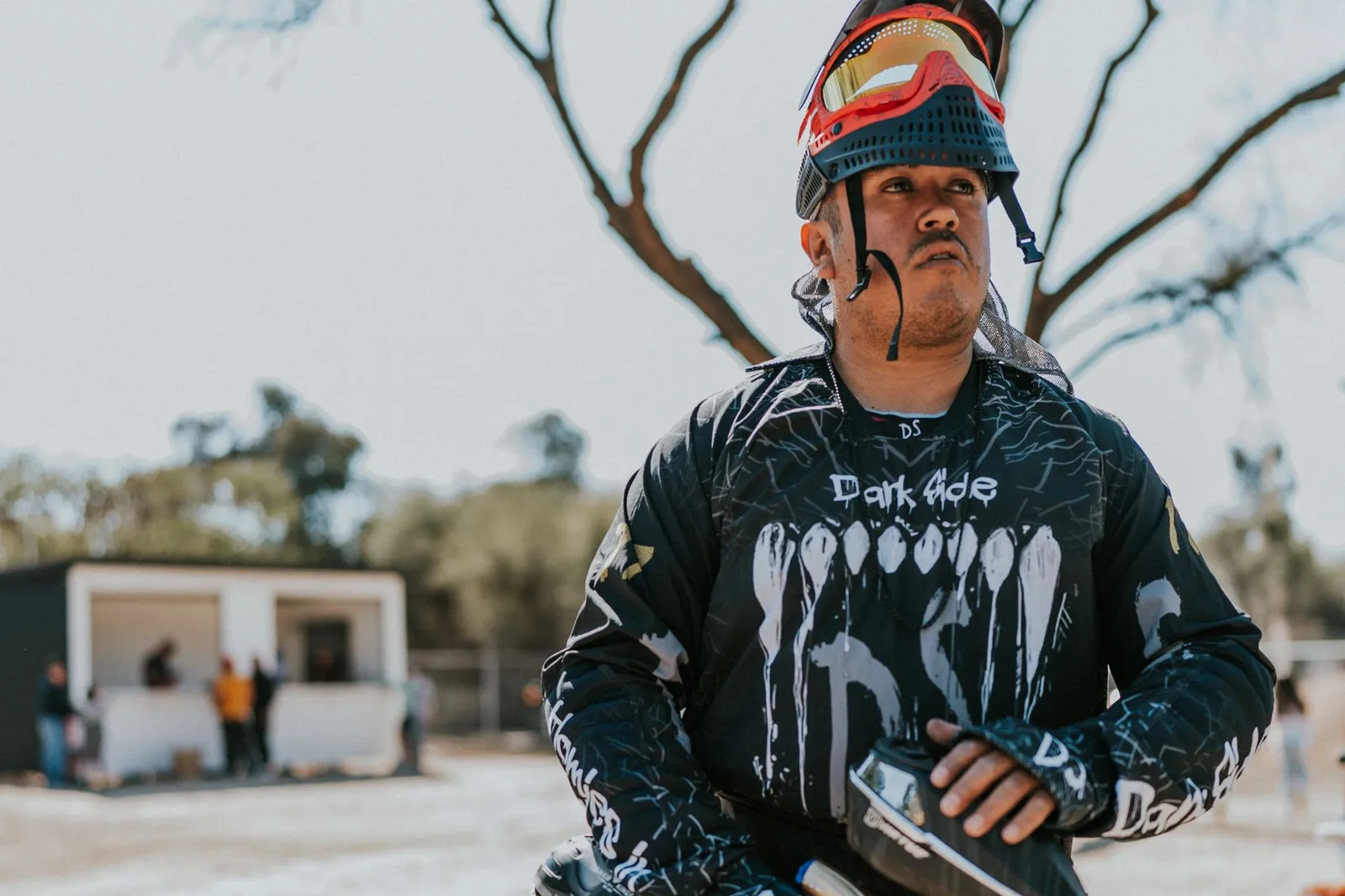 Joueur de paintball en maillot noir tenant son lanceur sur un terrain en extérieur