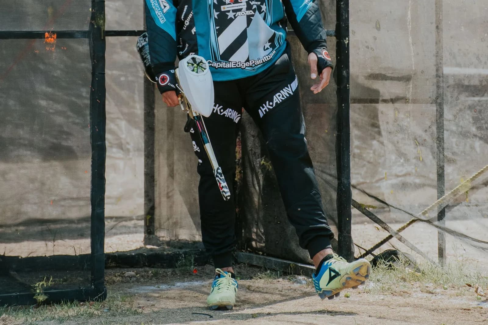 Joueur de paintball en maillot et masque à l'entrée grillagée d'un terrain