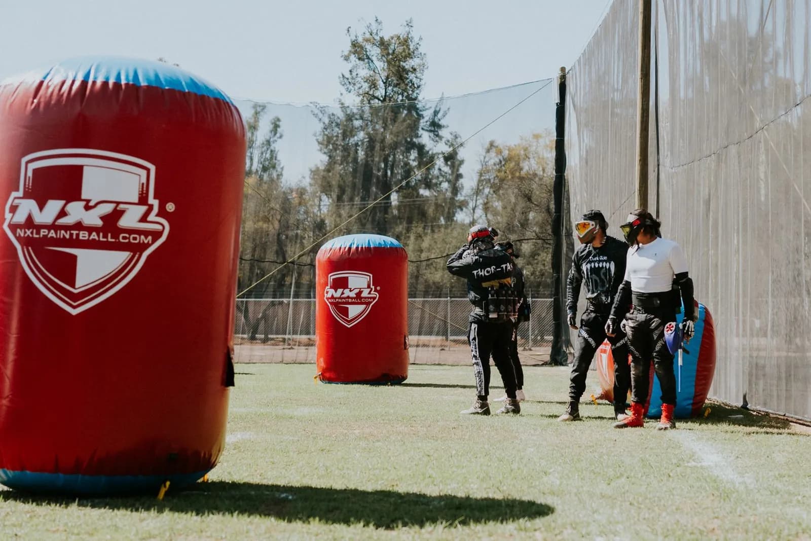 Terrain de paintball avec obstacles gonflables et joueurs, entouré de filets de protection