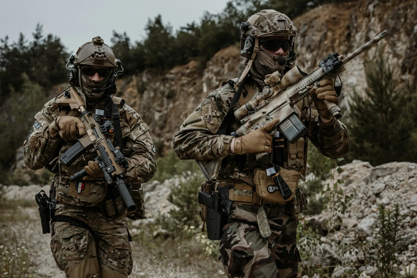 Deux joueurs d'airsoft équipés de casques et de gilets progressant dans une ancienne carrière rocheuse