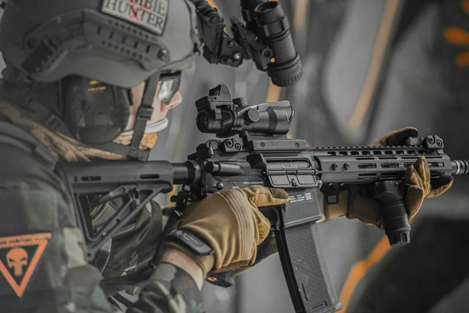 Gros plan sur un joueur d'airsoft en intérieur tenant une réplique AEG équipée d'un viseur point rouge