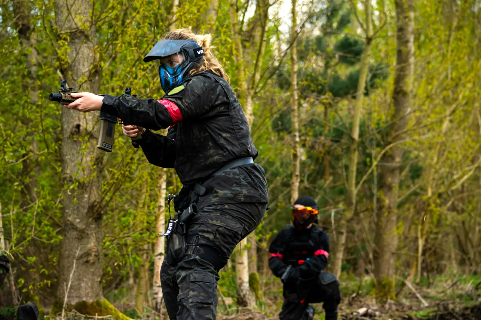 Joueuse de paintball équipée d'un masque, lanceur tendu, progressant dans un sous-bois