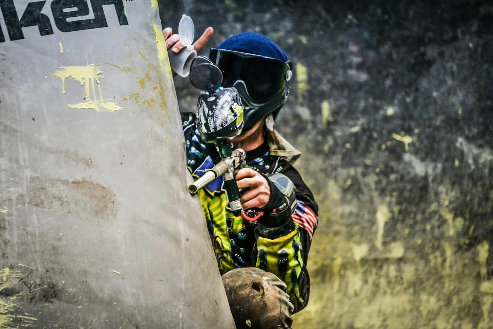 Joueur de paintball équipé d'un masque, à l'abri derrière un obstacle gonflable taché de peinture, lanceur en main