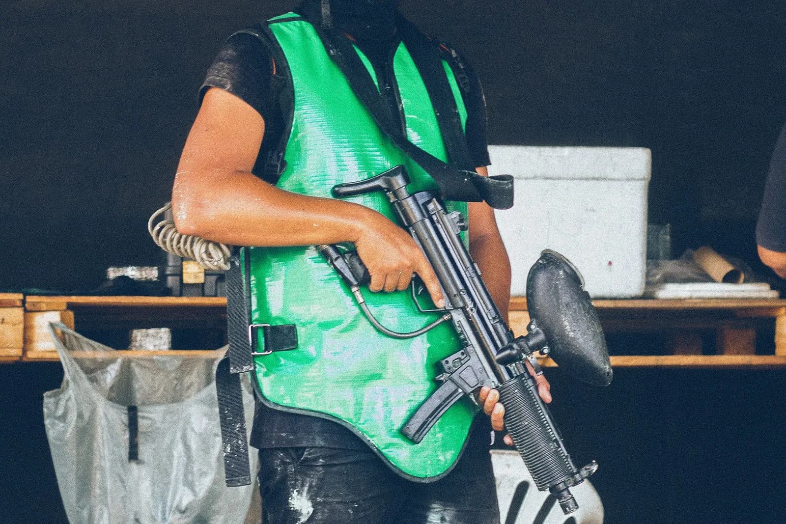 Joueur de paintball en chasuble verte tenant un lanceur près d'un poste de matériel