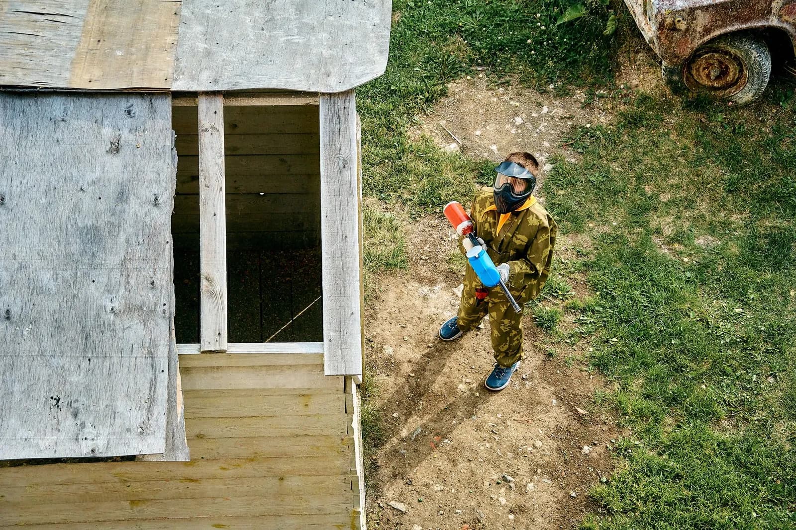 Vue aérienne d'un joueur de paintball en tenue camouflage avec son lanceur près d'une cabane