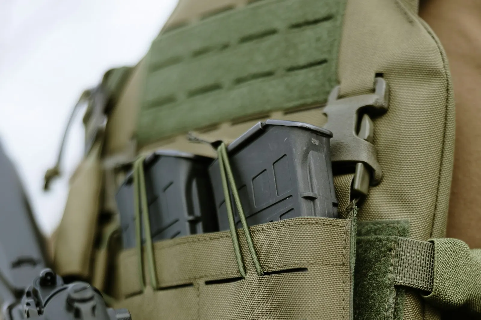 Deux chargeurs d'airsoft noirs rangés dans les poches d'un gilet porte-plaques vert olive