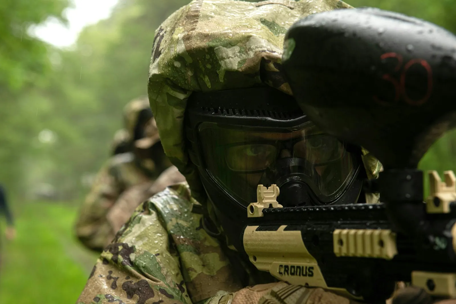 Joueur de paintball en tenue camouflage à capuche visant avec son lanceur et son masque
