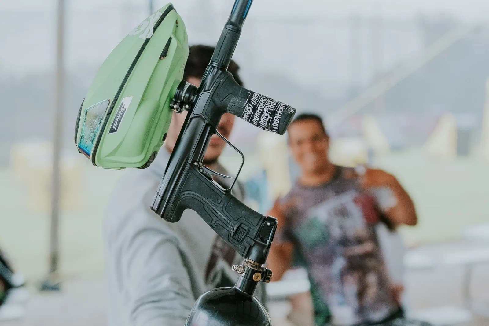 Joueur de paintball tenant un lanceur équipé d'une trémie verte et d'une bouteille d'air