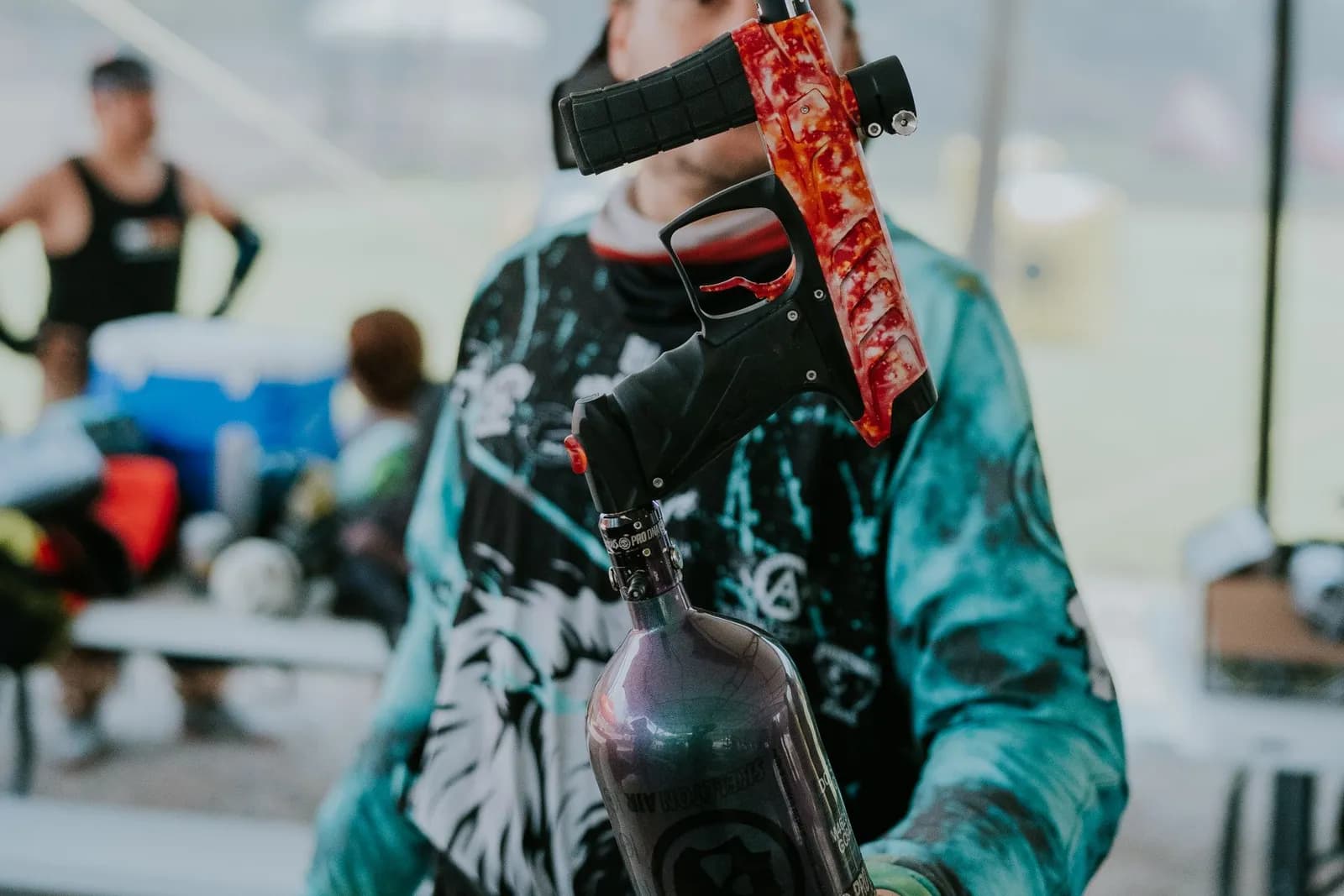 Joueur de paintball masqué tenant un lanceur électronique rouge et noir sous une tente