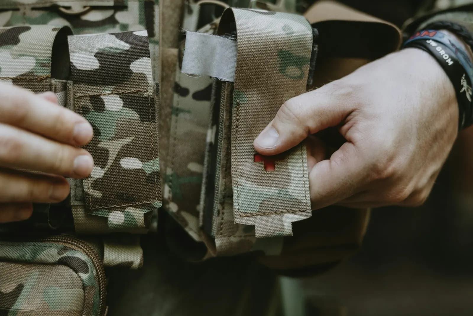 Mains d'un joueur d'airsoft ouvrant une poche médicale camouflage fixée sur son gilet