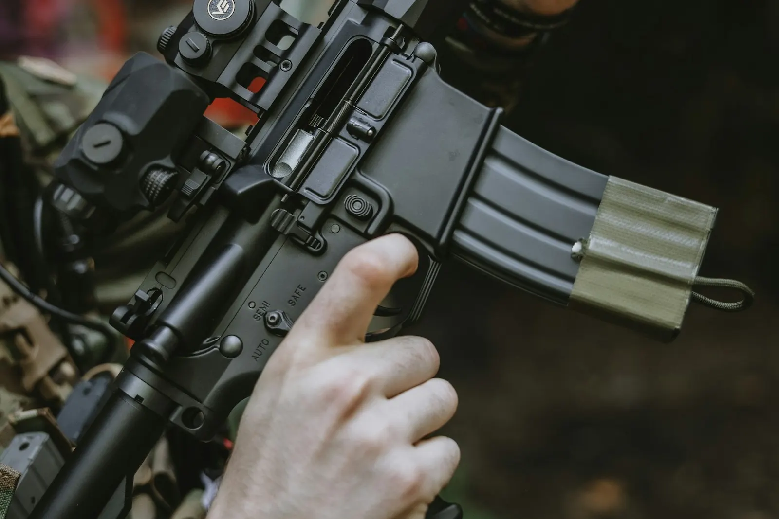 Gros plan sur les mains d'un joueur d'airsoft tenant une réplique noire, index le long du pontet près du chargeur