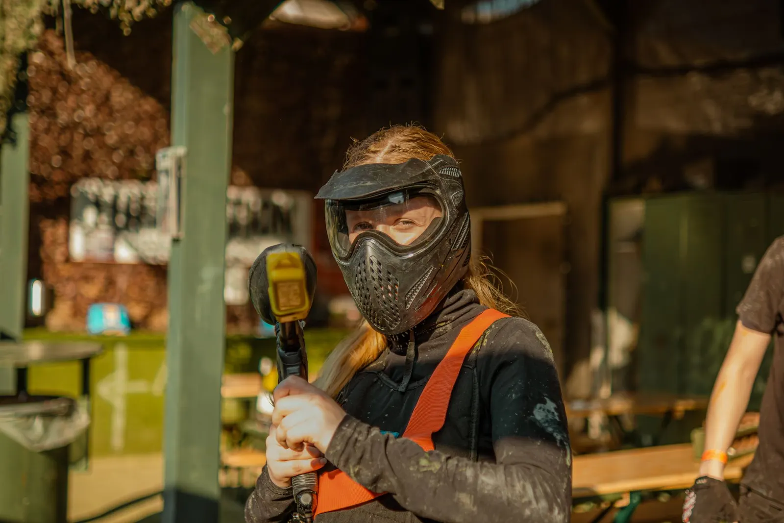 Joueuse de paintball en masque et gilet orange tenant un lanceur jaune dans l'espace d'accueil d'un centre