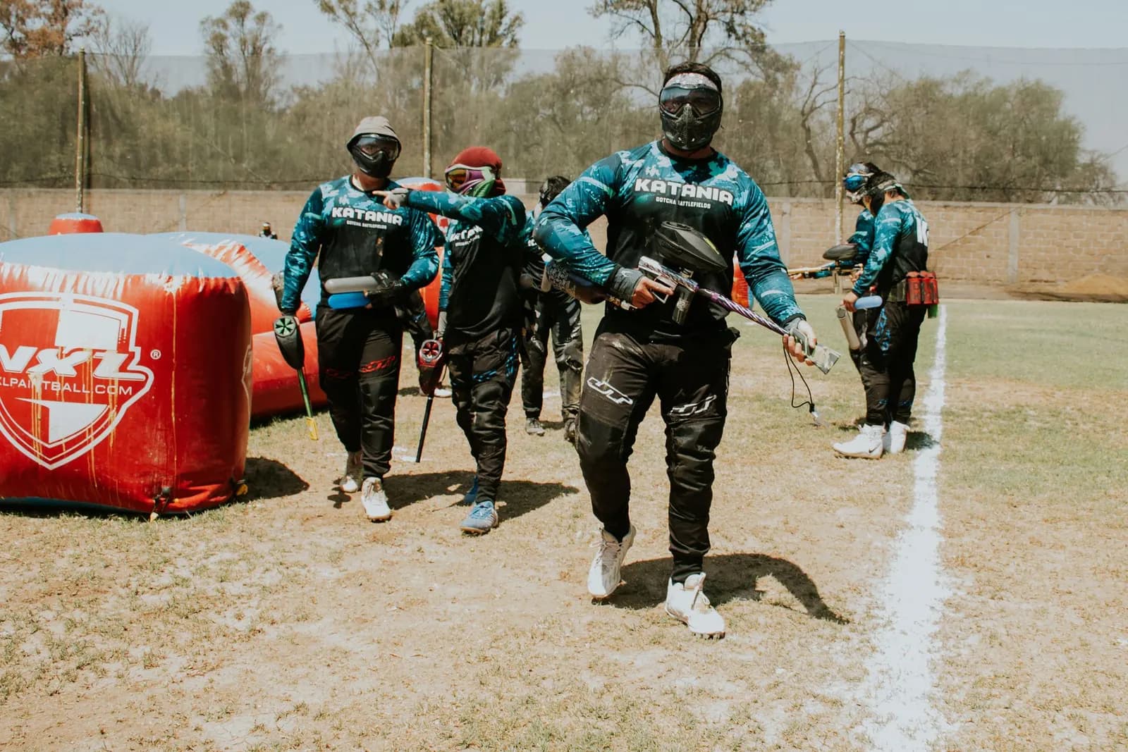 Groupe de joueurs de paintball en tenue et masques entrant sur un terrain équipé d'obstacles gonflables
