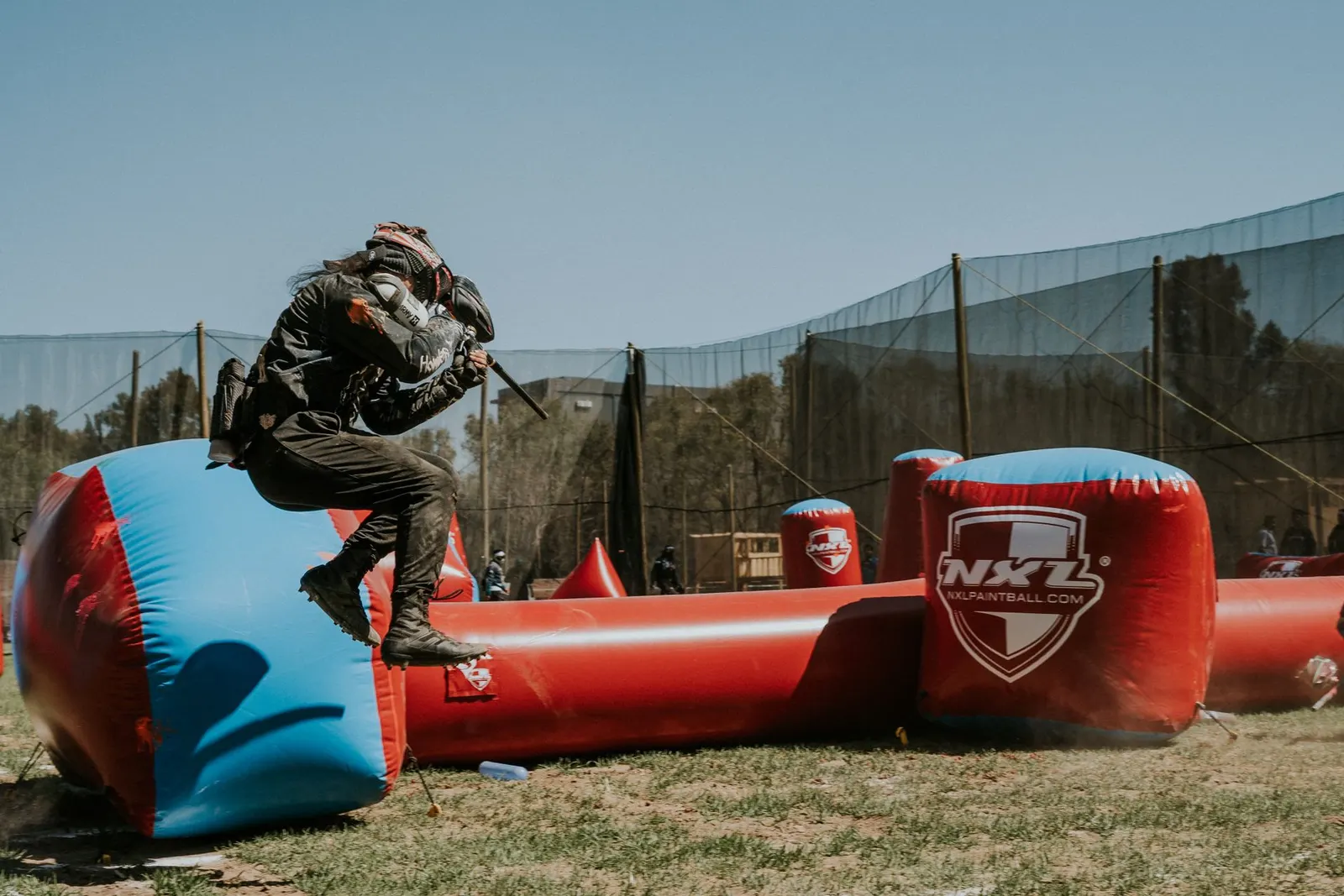 Joueur de paintball sautant par-dessus un obstacle gonflable bleu et rouge pendant une partie