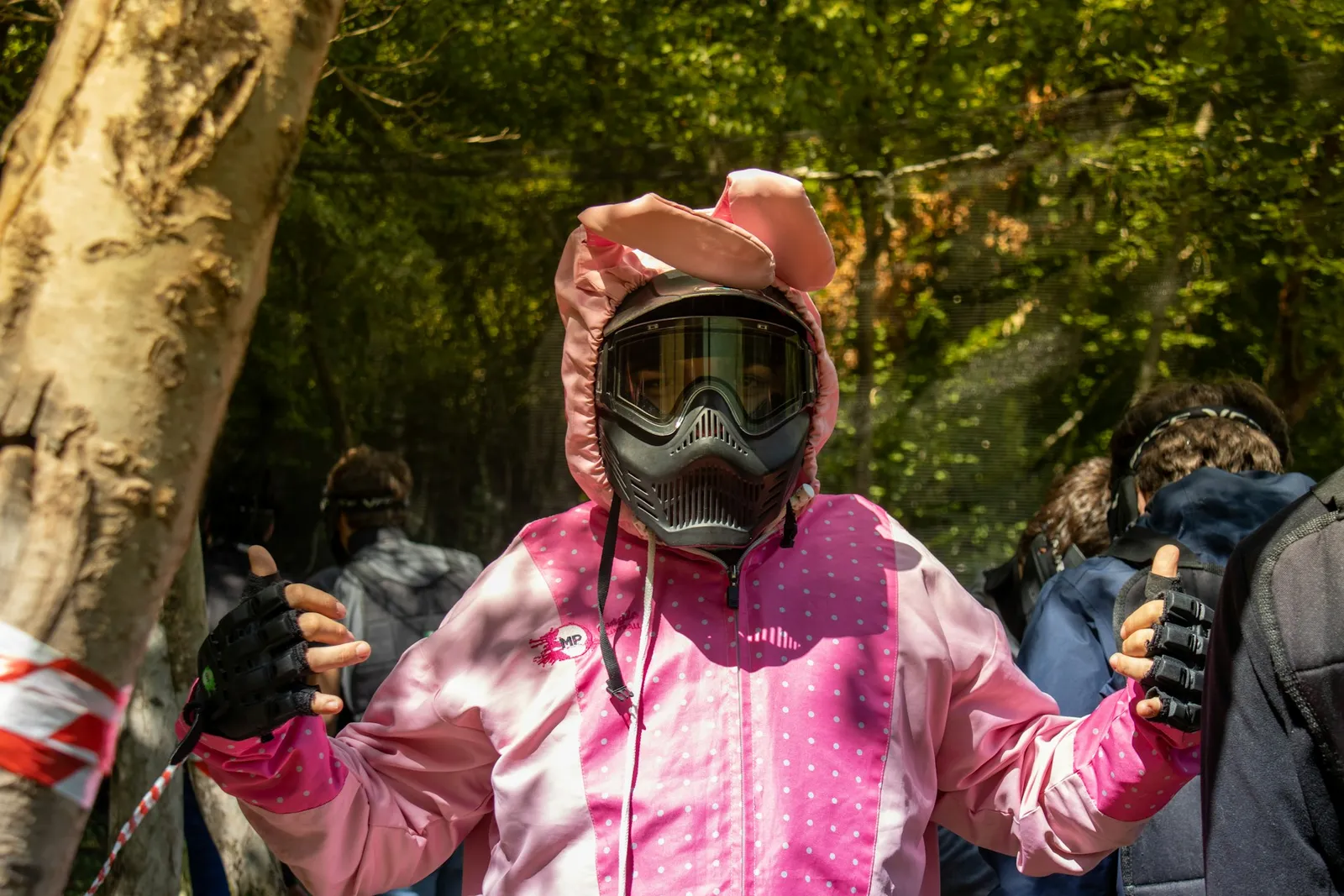 Joueuse de paintball en combinaison rose et masque, entourée d'autres joueurs en sous-bois