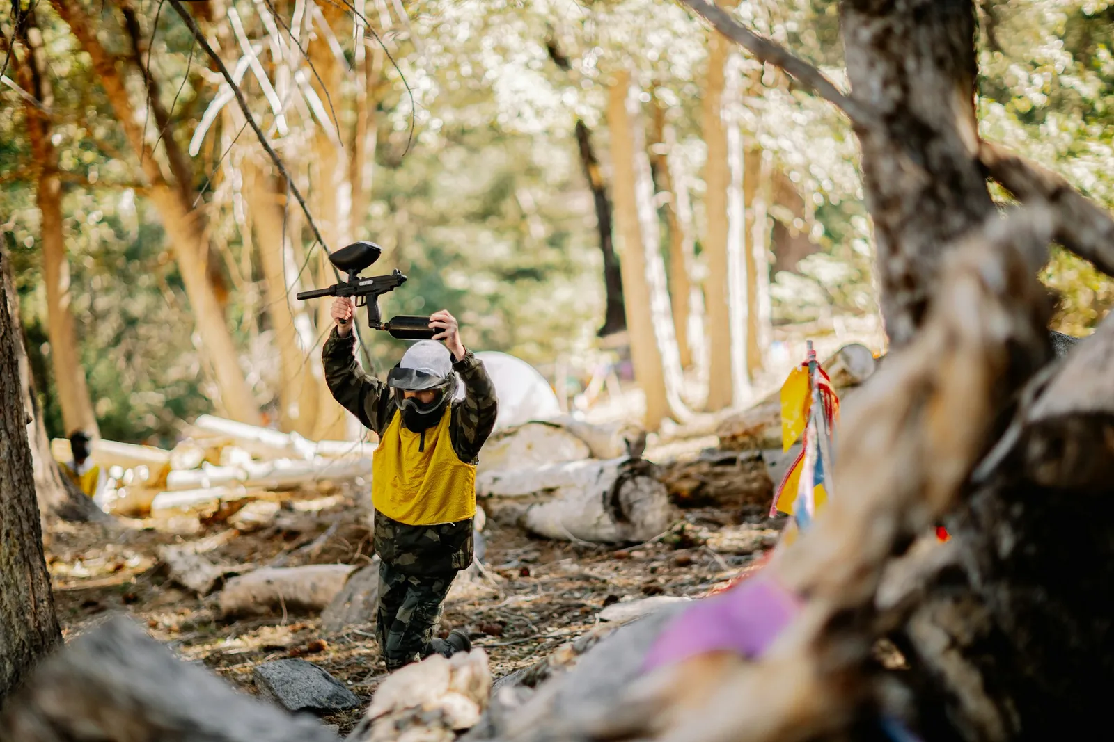 Joueur de paintball éliminé levant son lanceur au-dessus de la tête dans un sous-bois