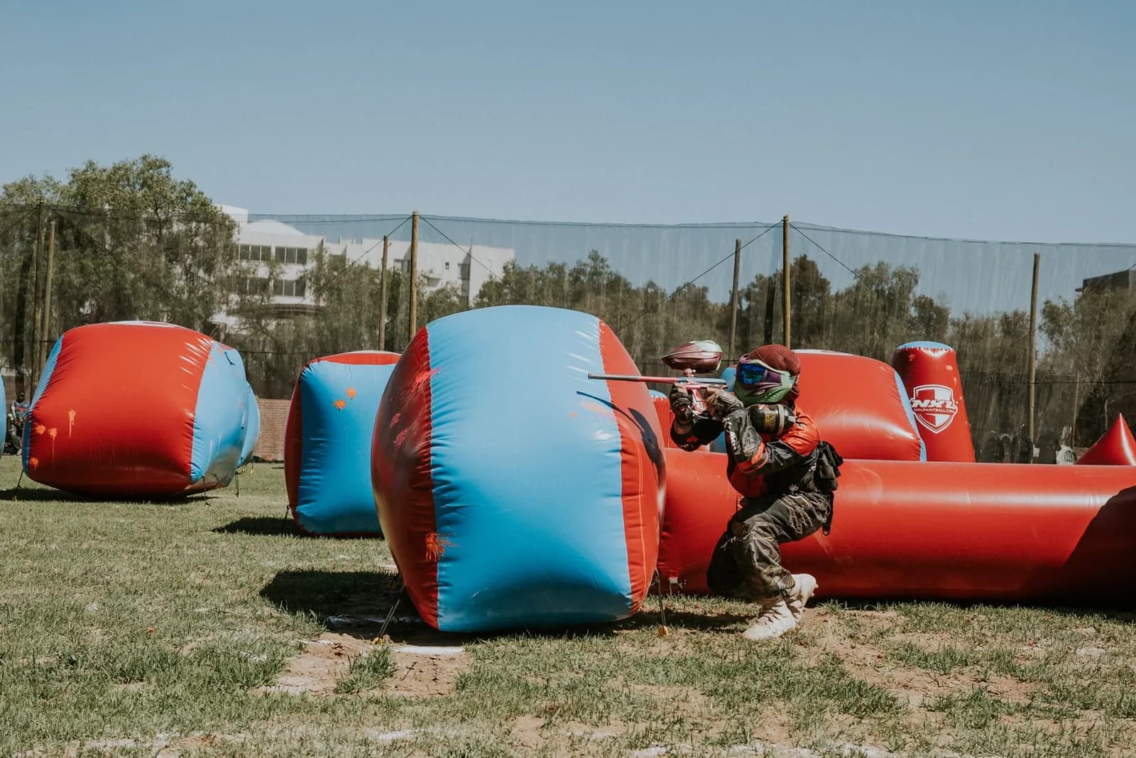 Joueur de paintball à genoux derrière des obstacles gonflables bleus et rouges, prêt à avancer