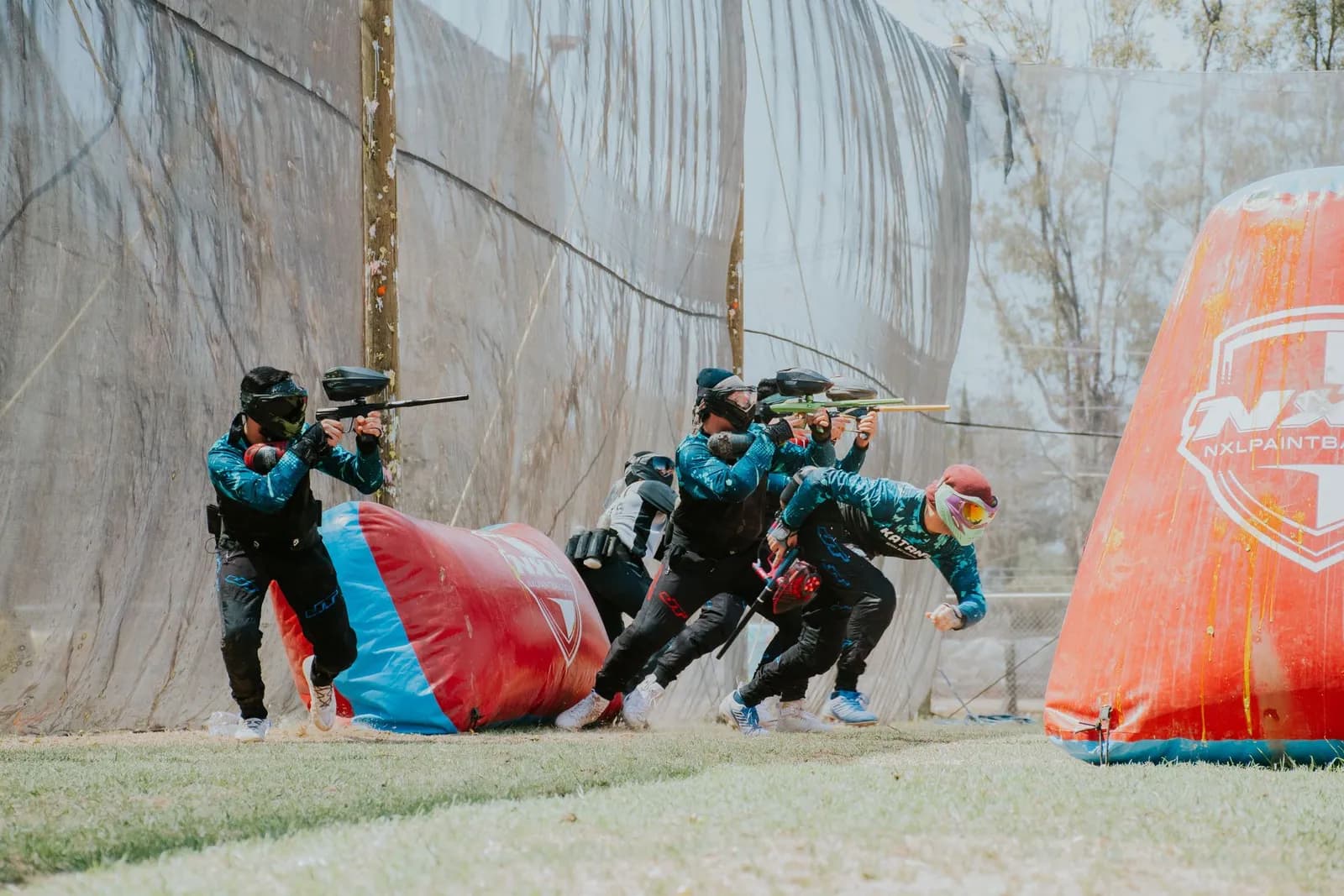 Équipe de joueurs de paintball avançant groupés derrière un obstacle gonflable, lanceurs en avant