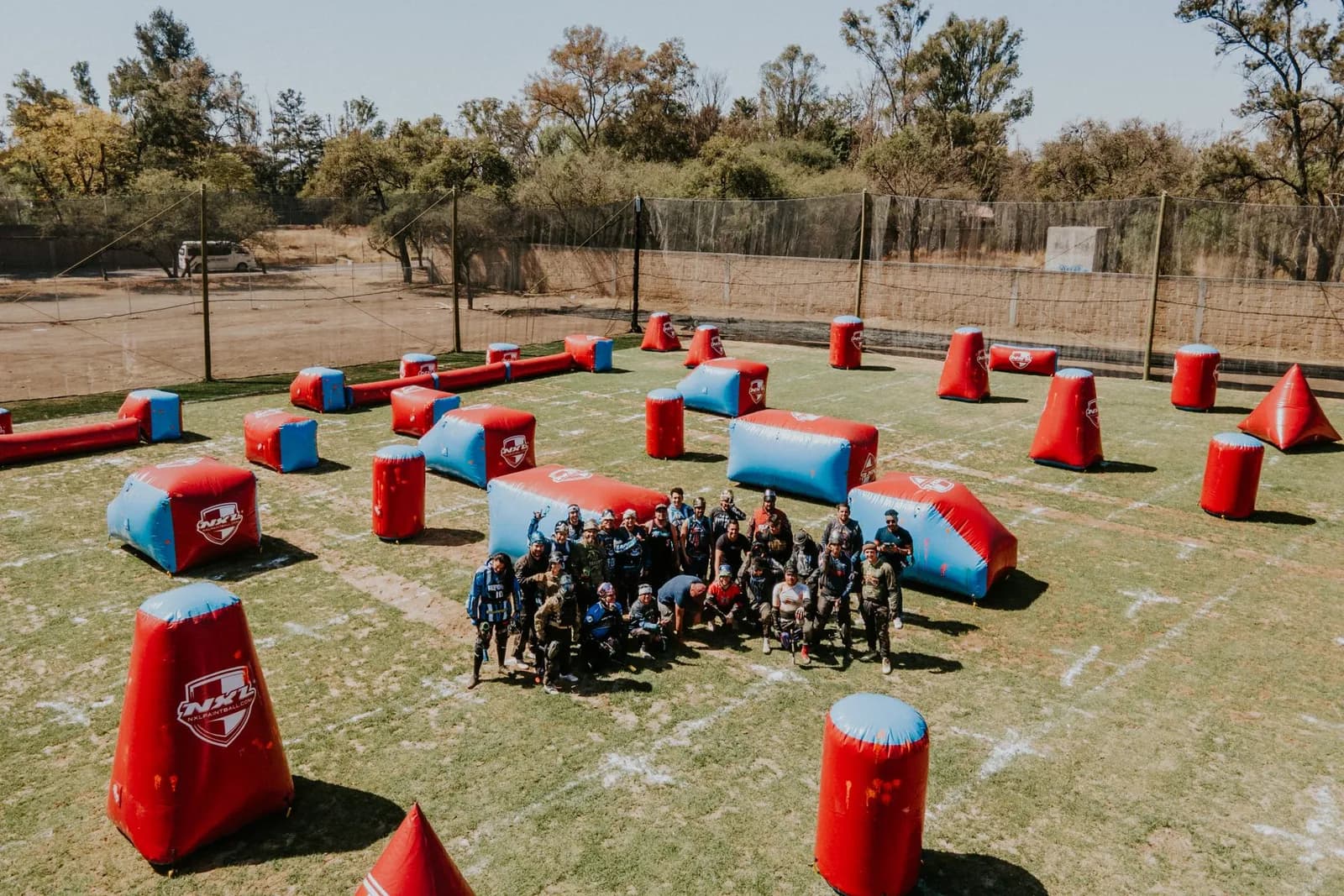 Grand groupe de joueurs de paintball réunis au milieu d'un terrain parsemé d'obstacles gonflables