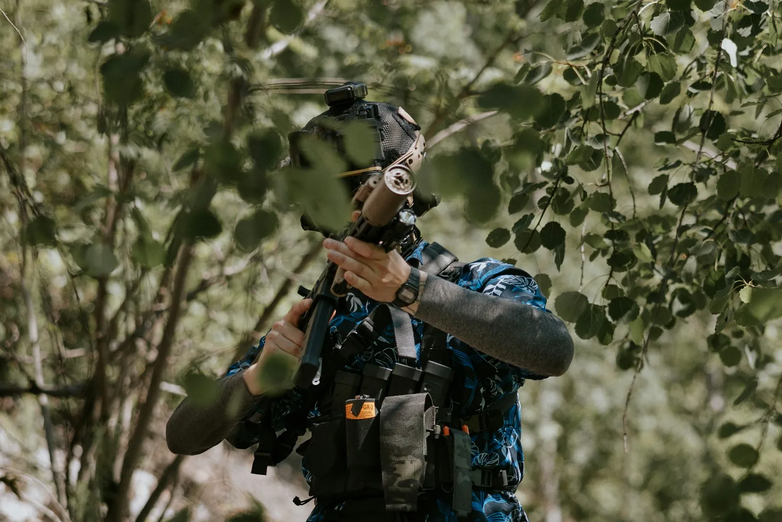 Joueur de paintball épaulant son lanceur dans une végétation dense
