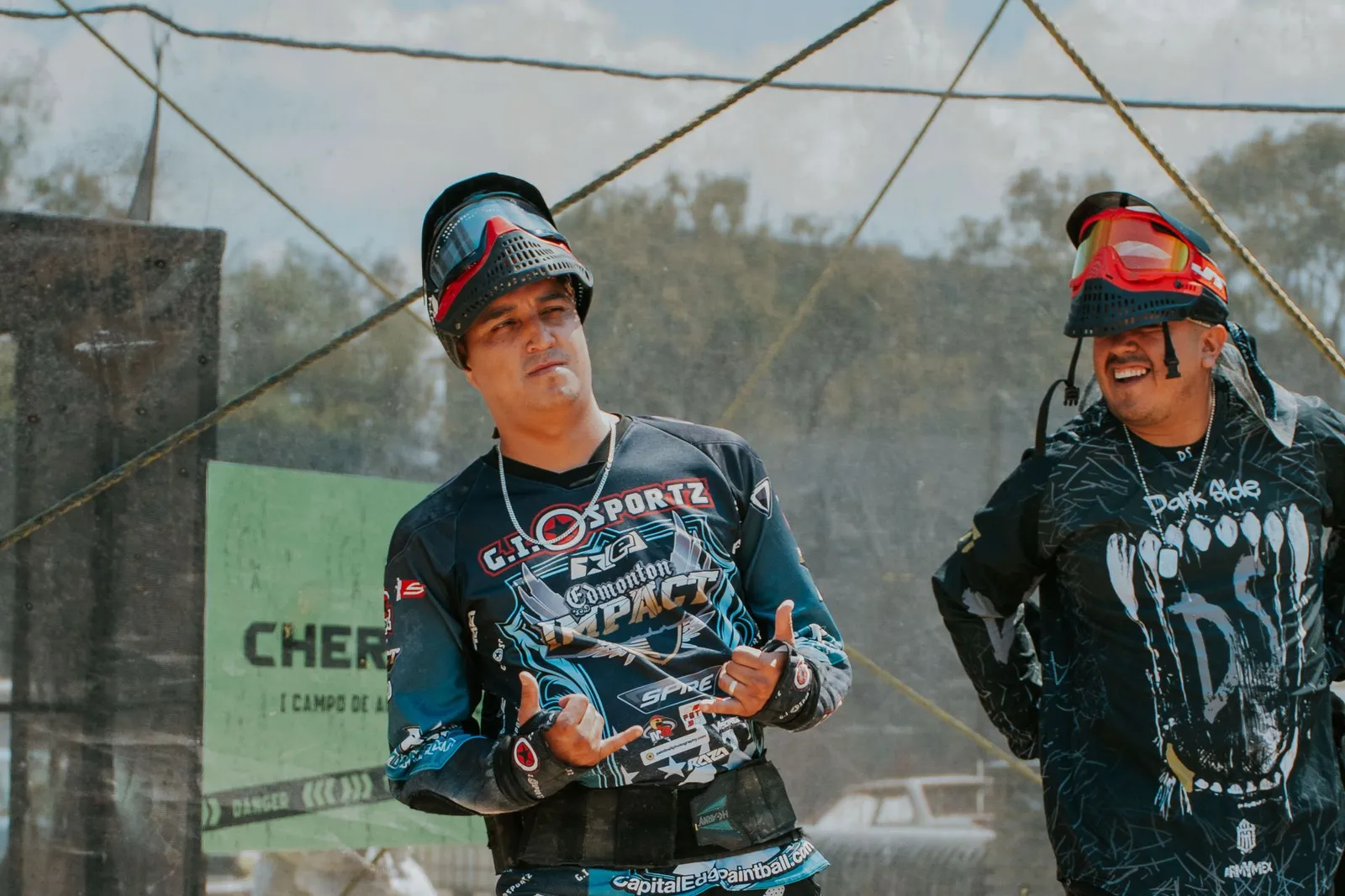 Deux joueurs de paintball souriants échangeant dans la zone de repos, masques relevés