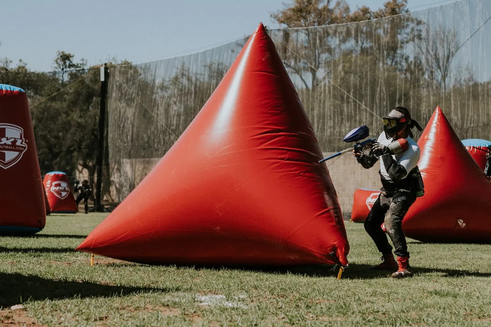 Joueur de paintball se déplaçant entre des pyramides gonflables rouges sur un terrain