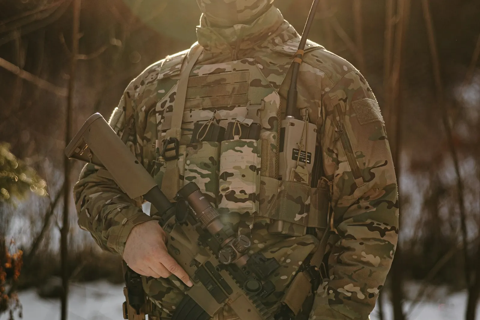 Joueur d'airsoft en tenue camouflage d'hiver avec radio sur le gilet et réplique en main, dans une forêt enneigée