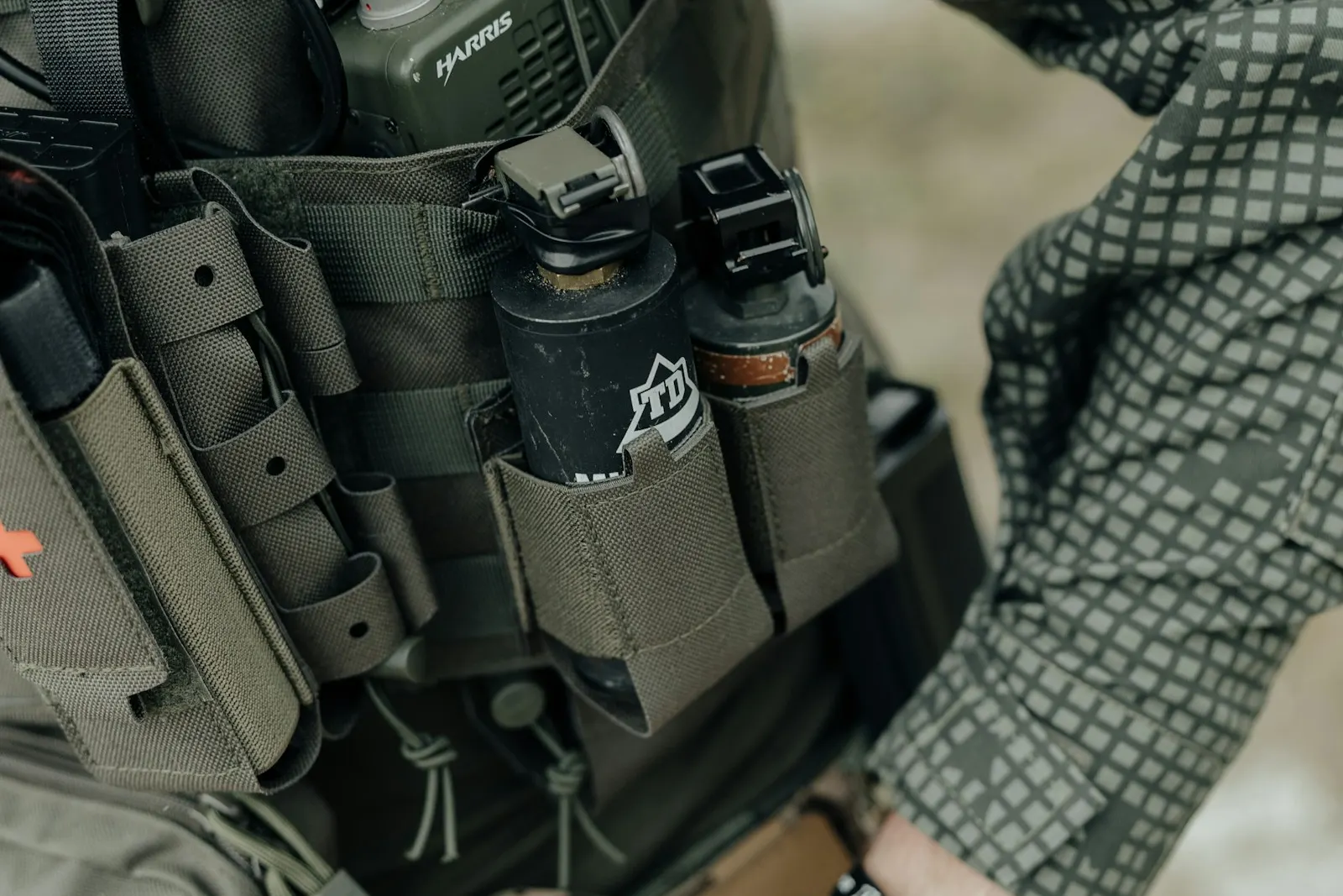 Gros plan sur un gilet tactique équipé d'une radio, de grenades et de poches, porté par un joueur d'airsoft