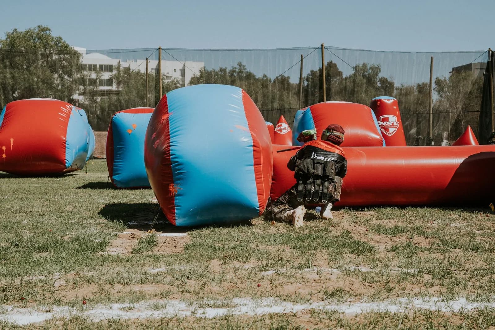 Joueur de paintball à genoux derrière un obstacle gonflable bleu et rouge sur un terrain