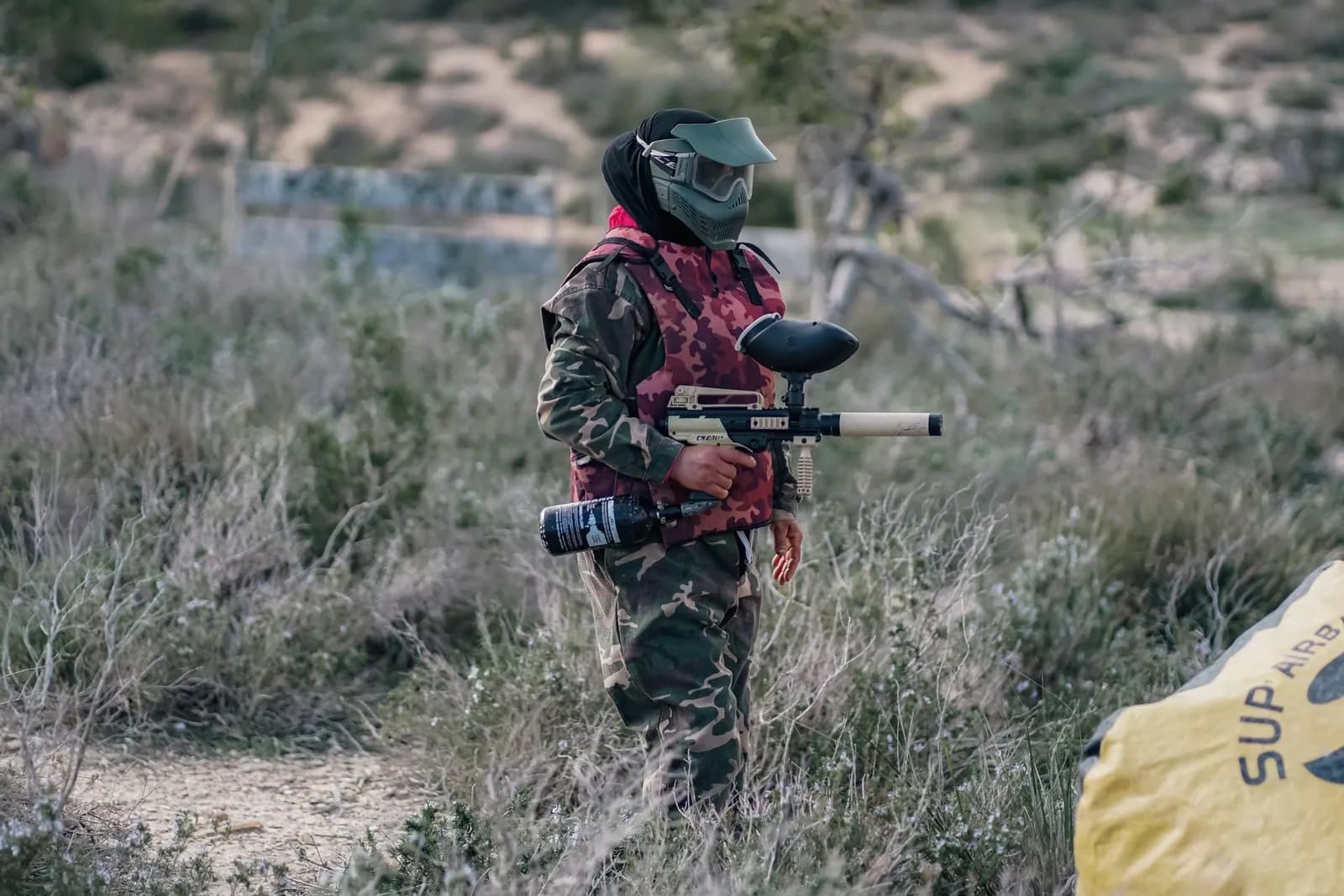 Joueuse de paintball en tenue camouflage et masque, lanceur de location en main, sur un terrain en extérieur
