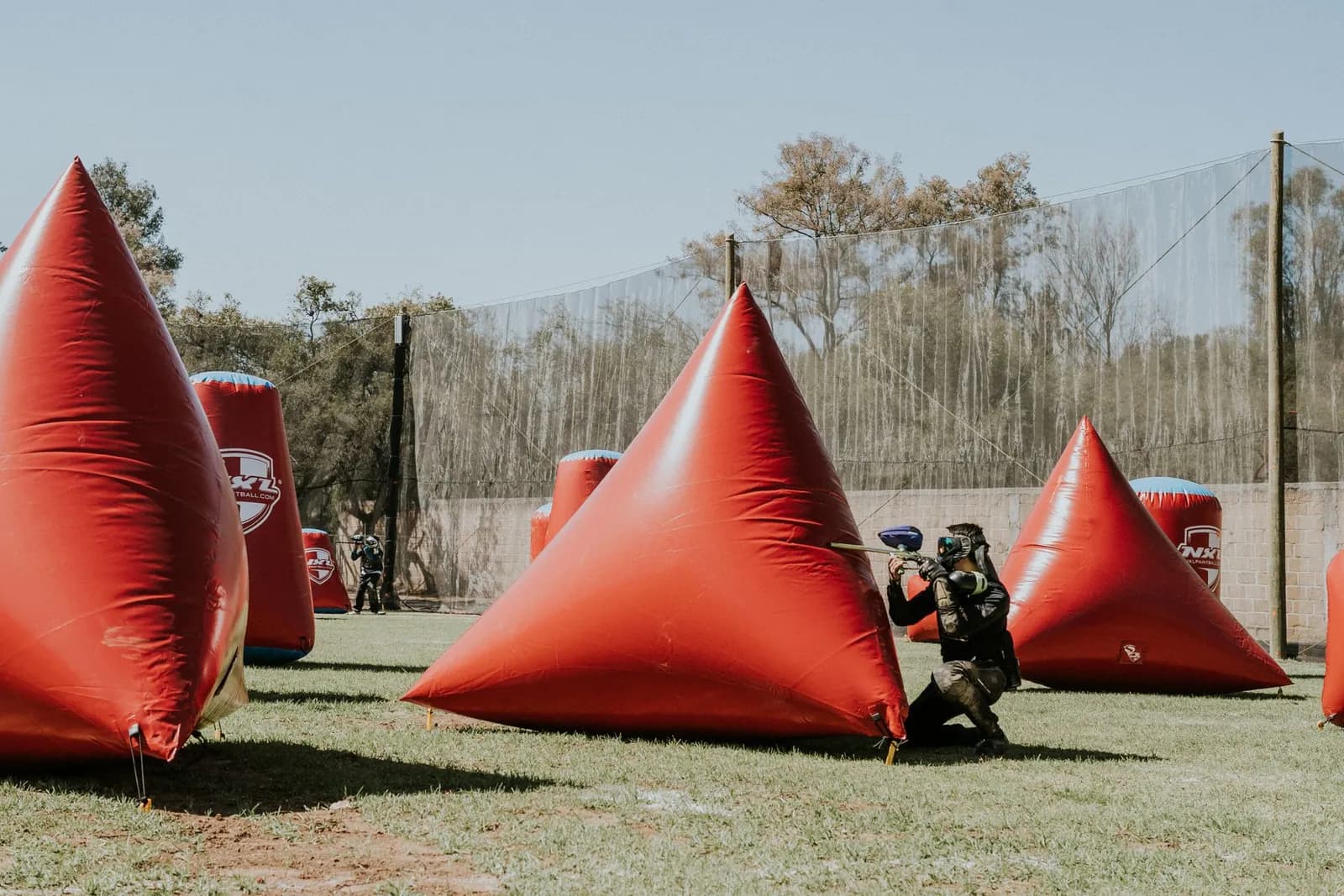 Joueur de paintball tirant derrière une pyramide gonflable rouge sur un terrain entouré de filets