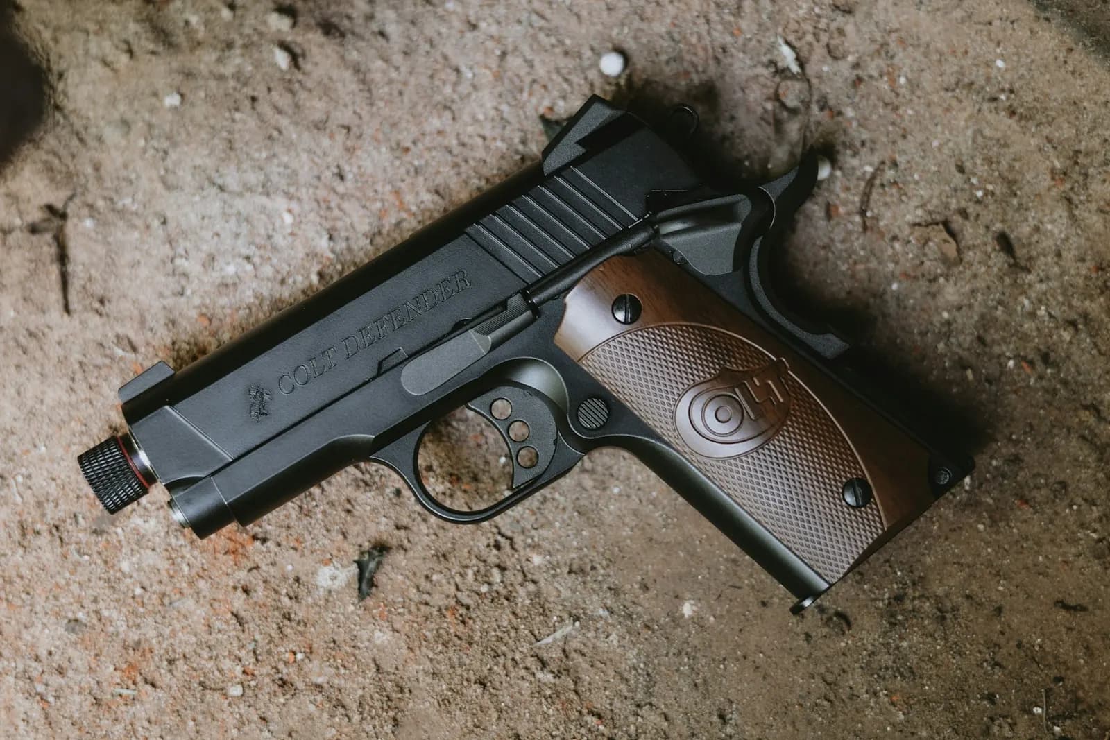 Pistolet d'airsoft à gaz GBB de type 1911 avec plaquettes de crosse en bois, posé sur un sol en terre
