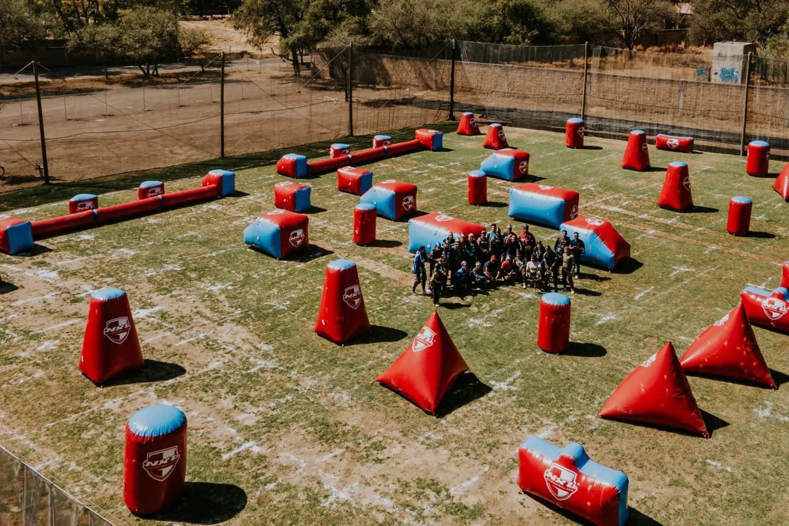 Vue aérienne d'un terrain de paintball avec obstacles gonflables, entouré de filets