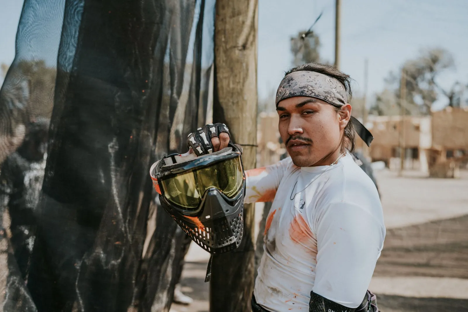 Joueur de paintball tenant son masque à la main, t-shirt taché de peinture, sur un terrain