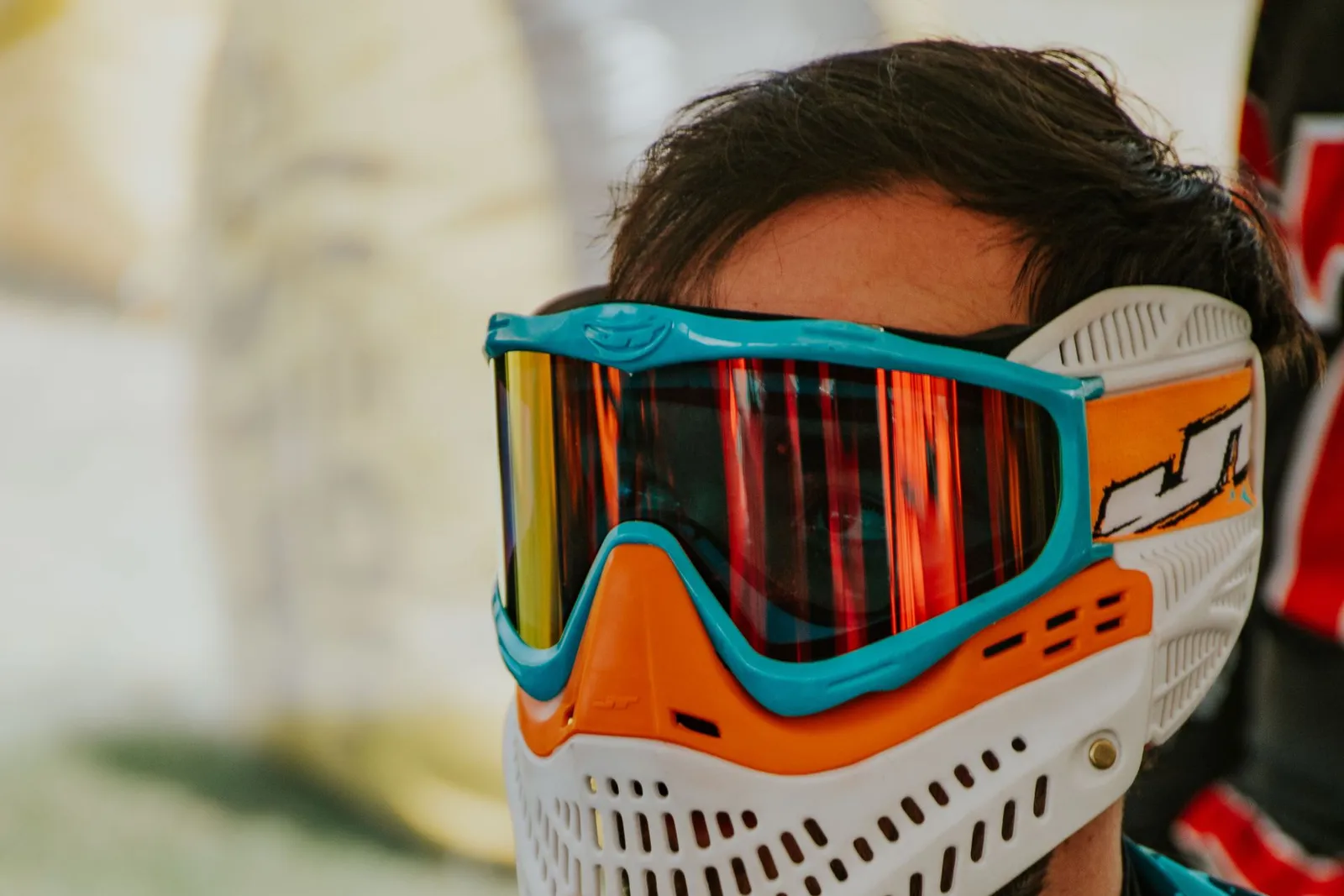 Joueur de paintball ajustant son masque intégral orange et blanc à écran miroir