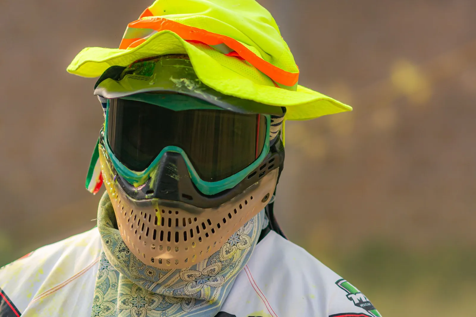 Joueur de paintball portant un masque, un bob fluo et un foulard protégeant le cou
