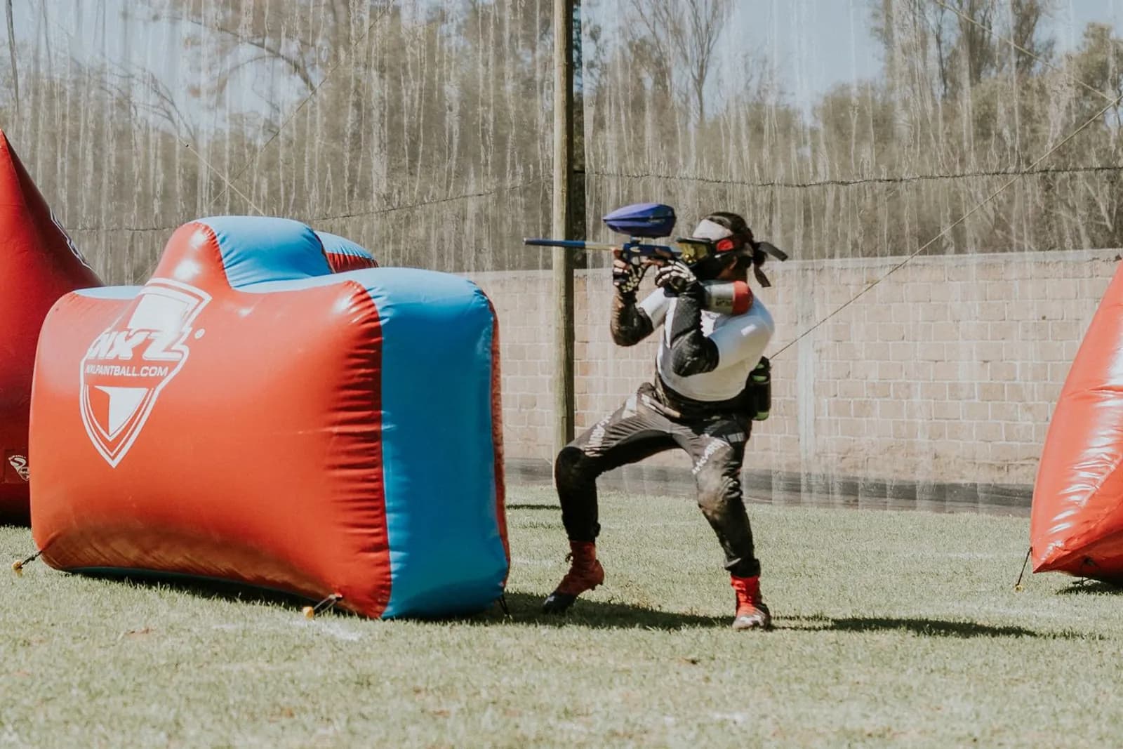 Joueur de paintball tirant à l'abri d'obstacles gonflables rouges et bleus sur un terrain de compétition