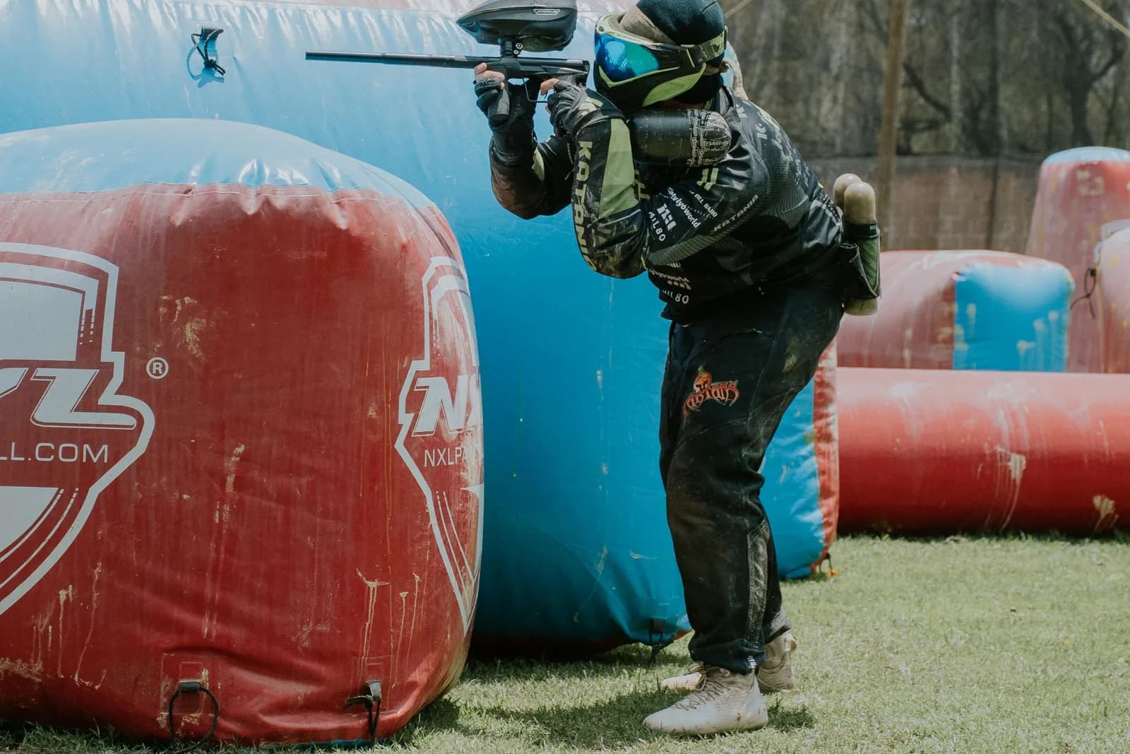 Joueur de paintball tirant derrière un obstacle gonflable bleu sur un terrain de compétition